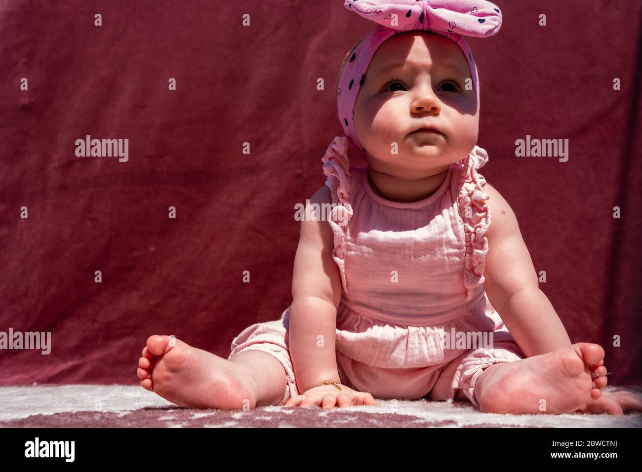 Cute little baby girl wear hat and sit on carpet at outside, looking at
