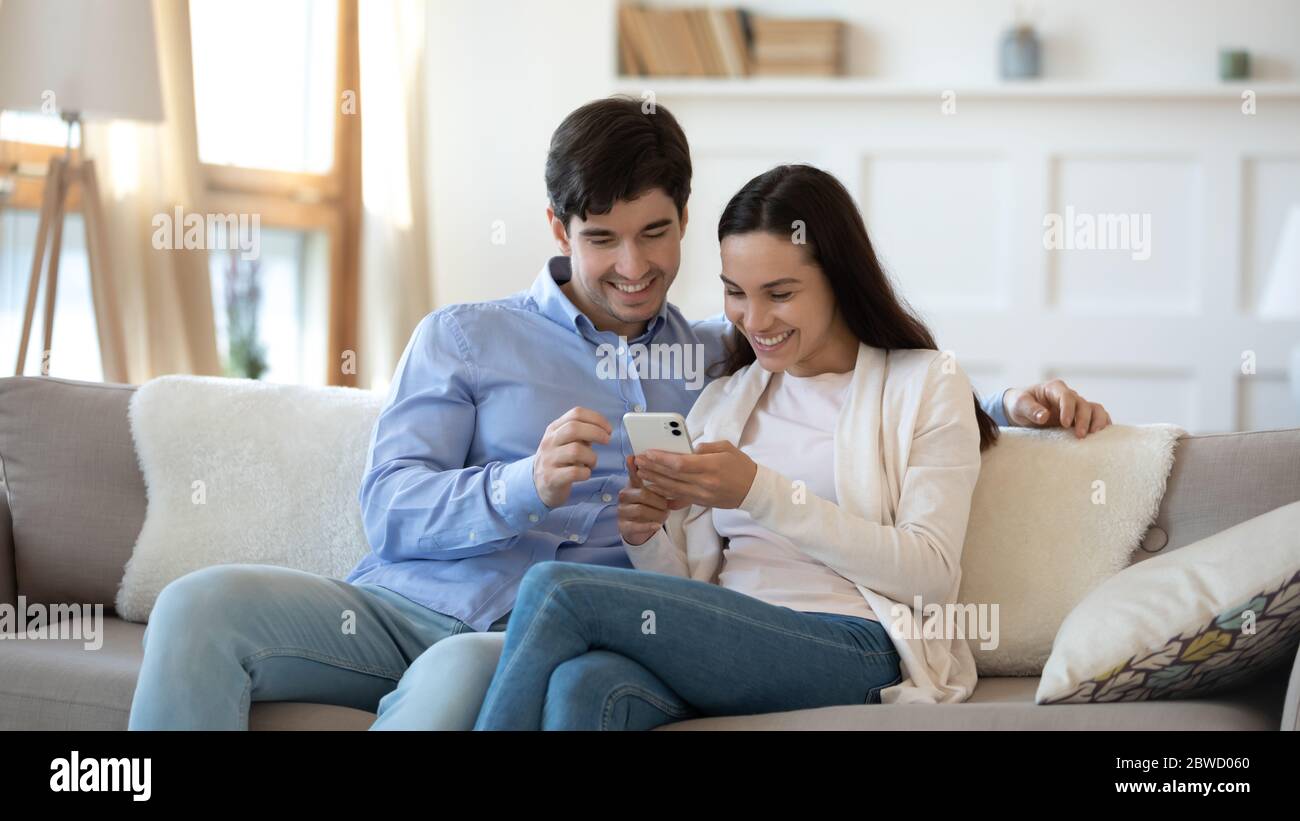 Happy couple rest on sofa using smartphone Stock Photo