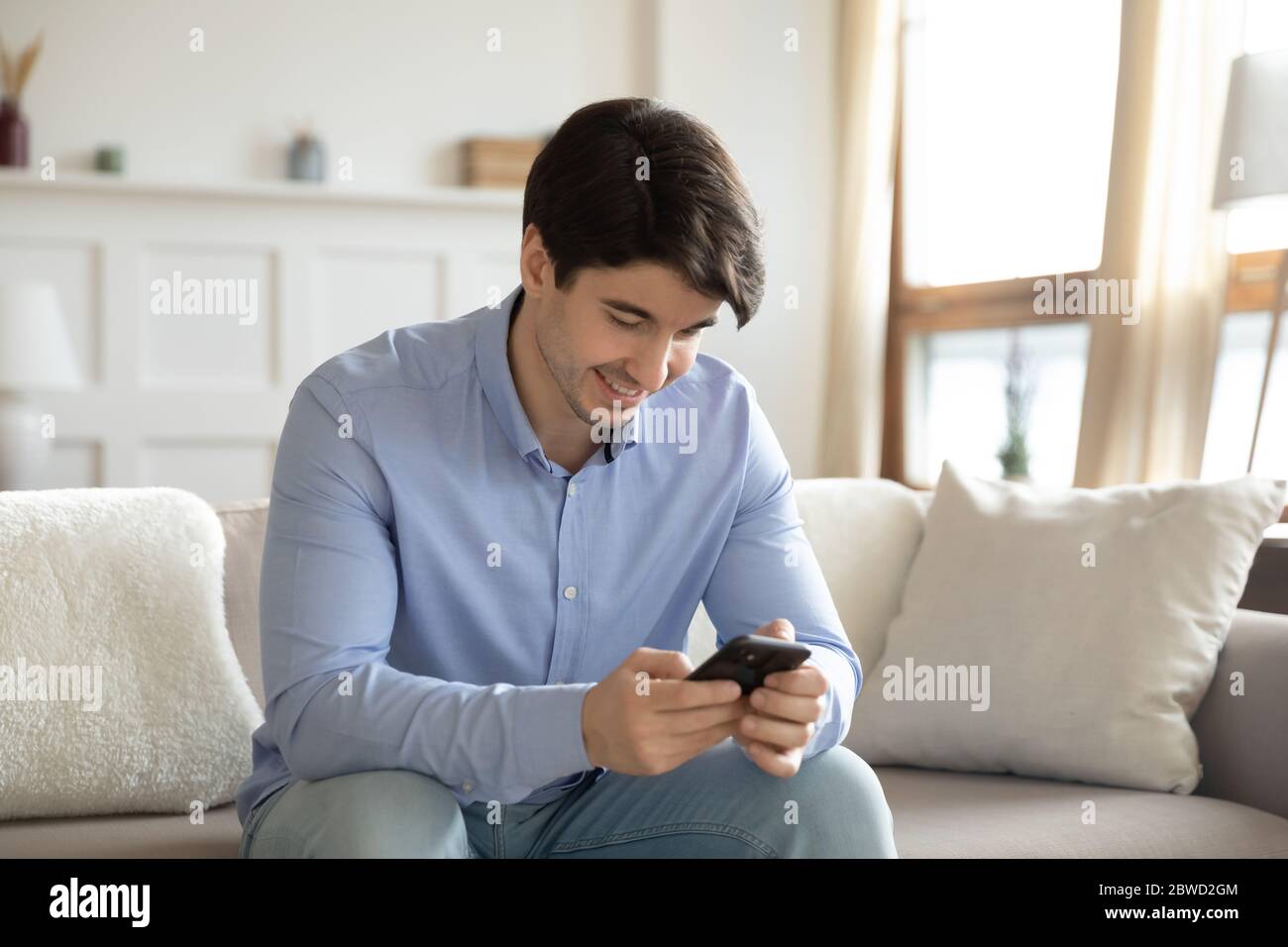 Smiling young man using modern smartphone at home Stock Photo