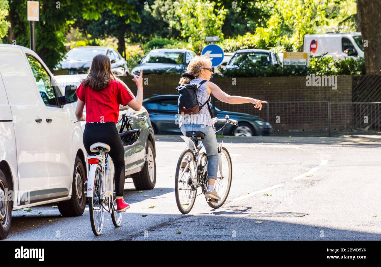 Adult woman and teenager cycling on road and signalling to turn right Stock Photo