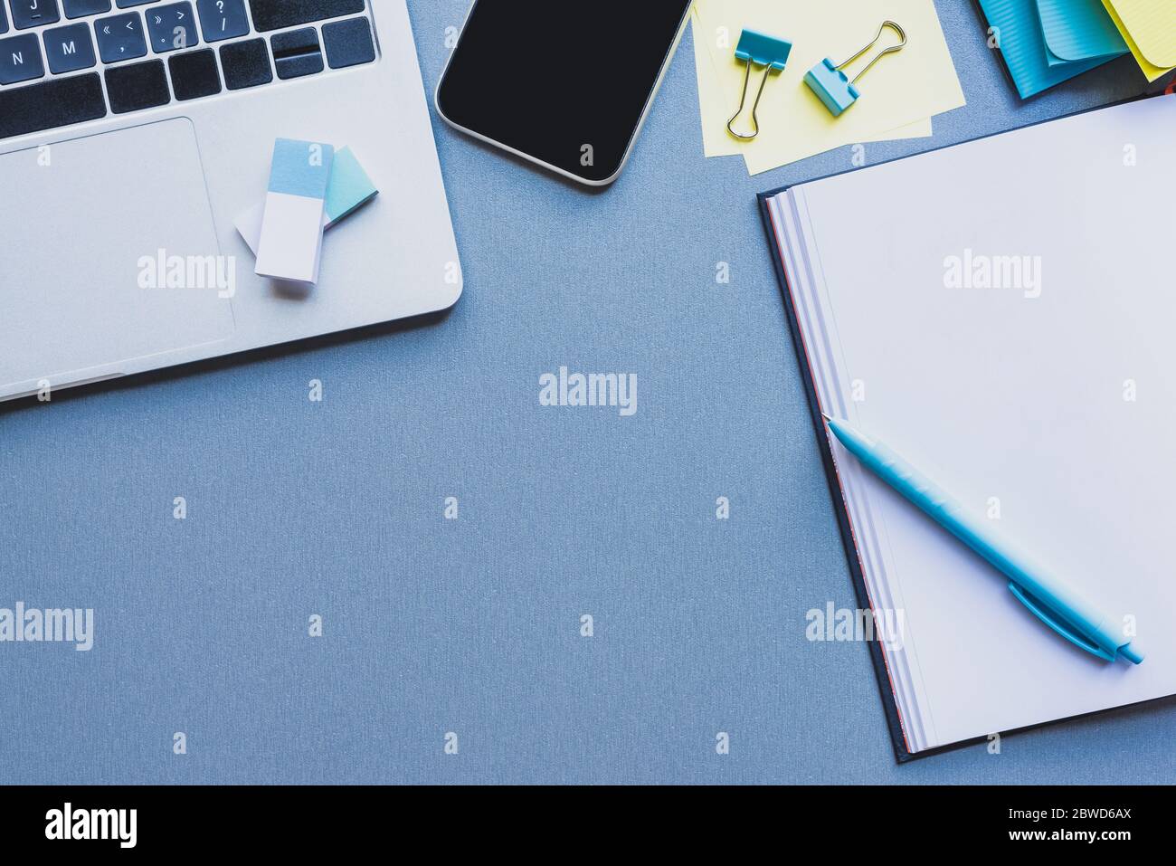 Top view of digital devices, stationery and open notebook on blue surface Stock Photo