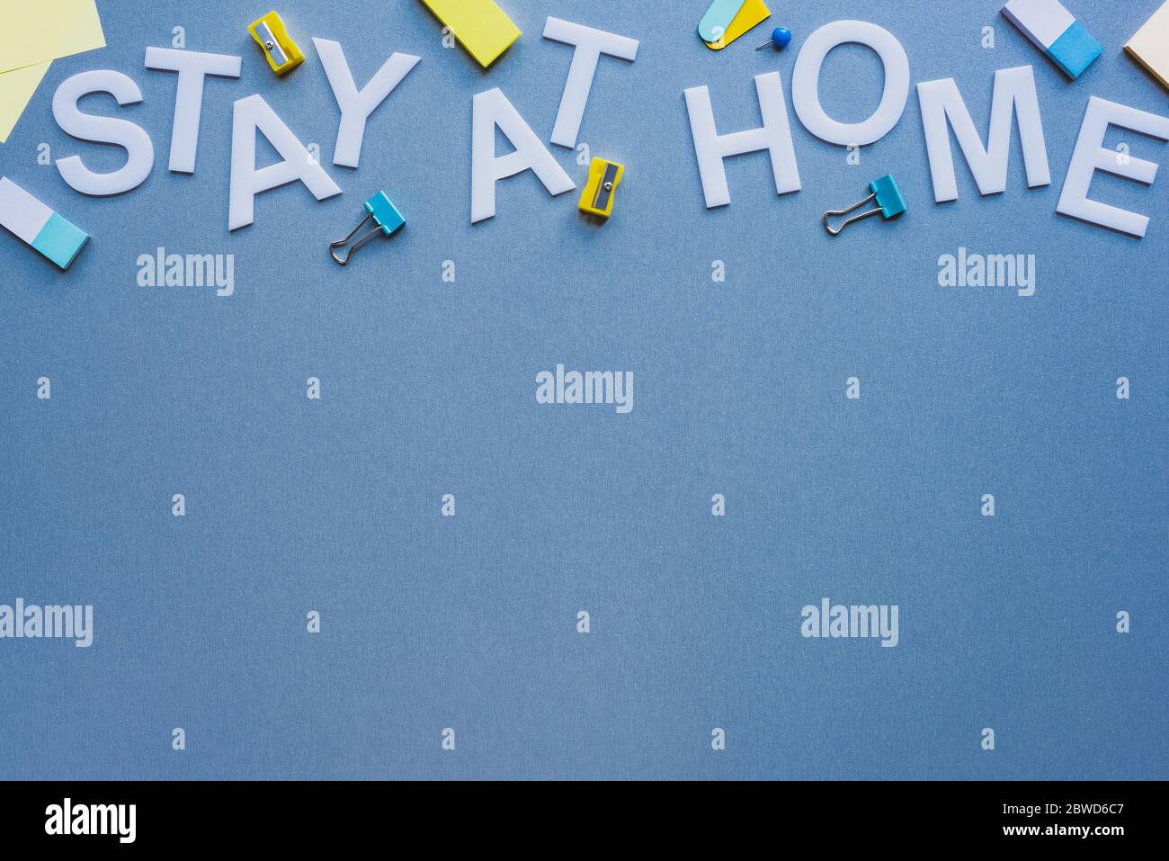 Top view of stay at home lettering near pencil sharpeners, erasers and binder clips on blue surface Stock Photo