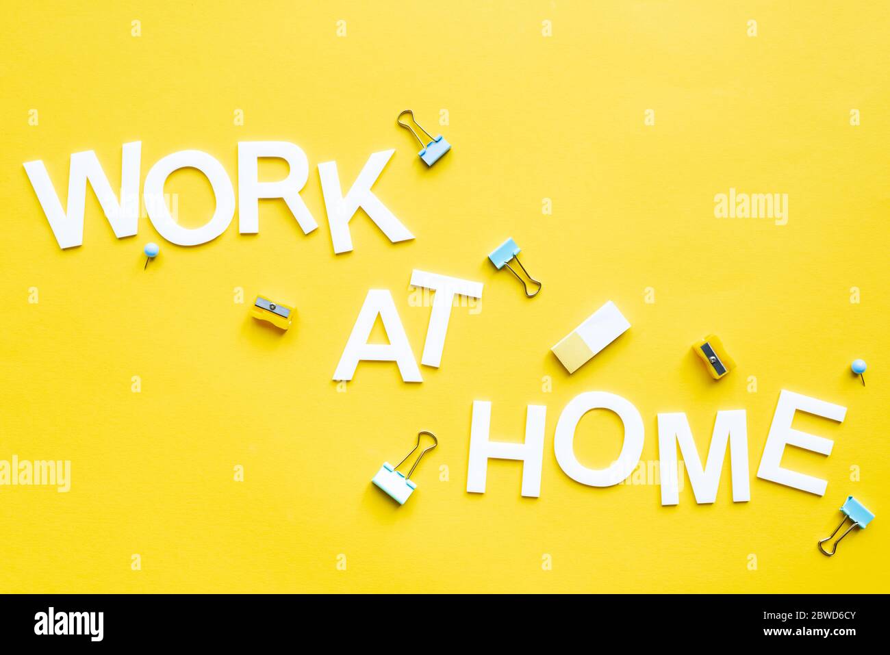 Top view of work at home lettering with pencil sharpeners, binder clips and eraser on yellow surface Stock Photo