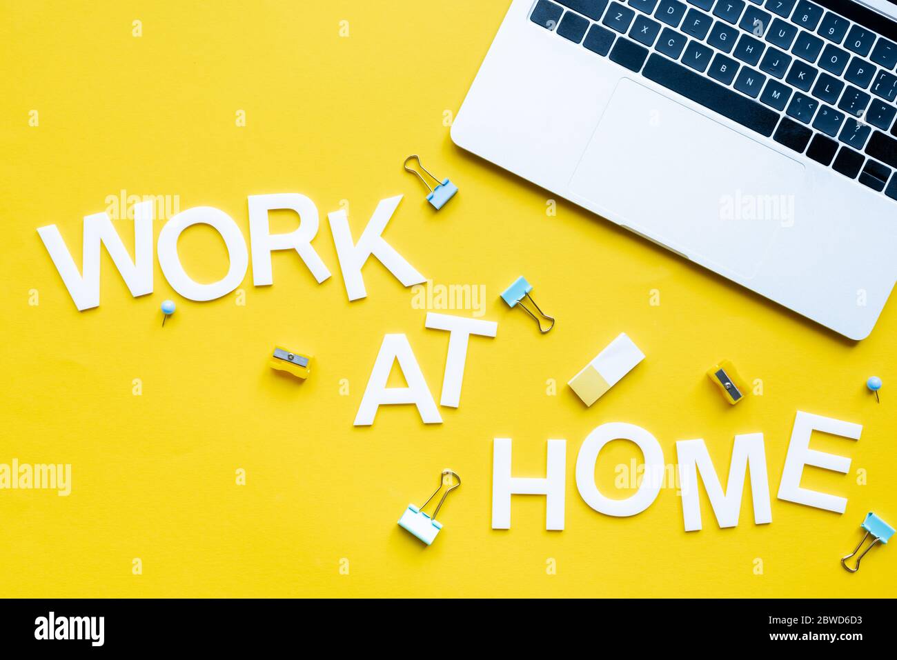 Top view of work at home lettering near laptop, binder clips and pencil sharpeners on yellow surface Stock Photo