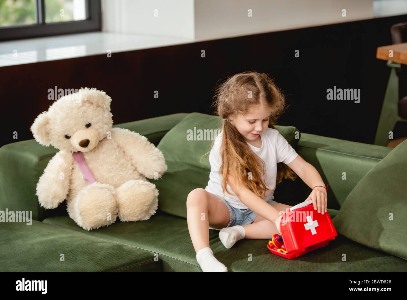 cute child touching toy first aid kit box near teddy bear while playing  doctor game Stock Photo - Alamy