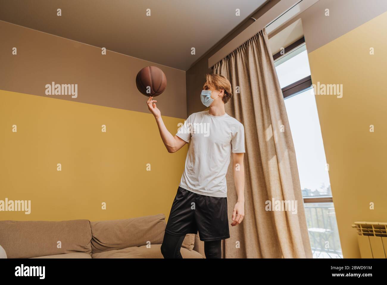 man in medical mask spinning basketball on finger at home Stock Photo ...