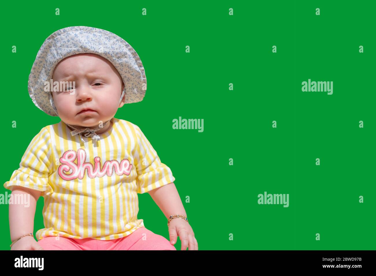 Cute baby girl wear adorable hat looking at camera make funny faces on green screen with text space Stock Photo