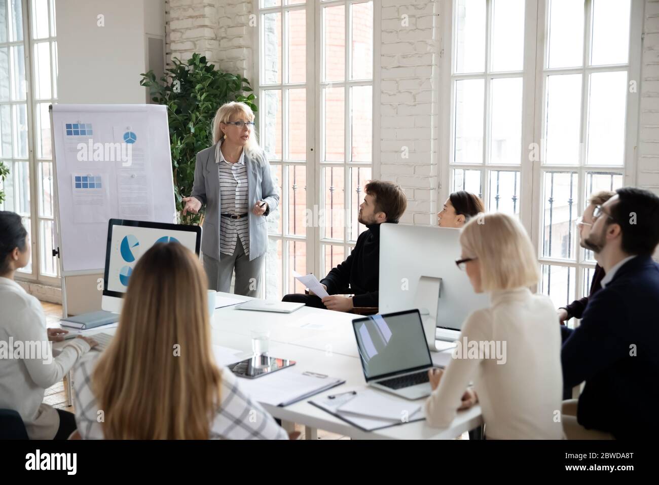 Focused young businesspeople listening to middle aged female lecturer. Stock Photo