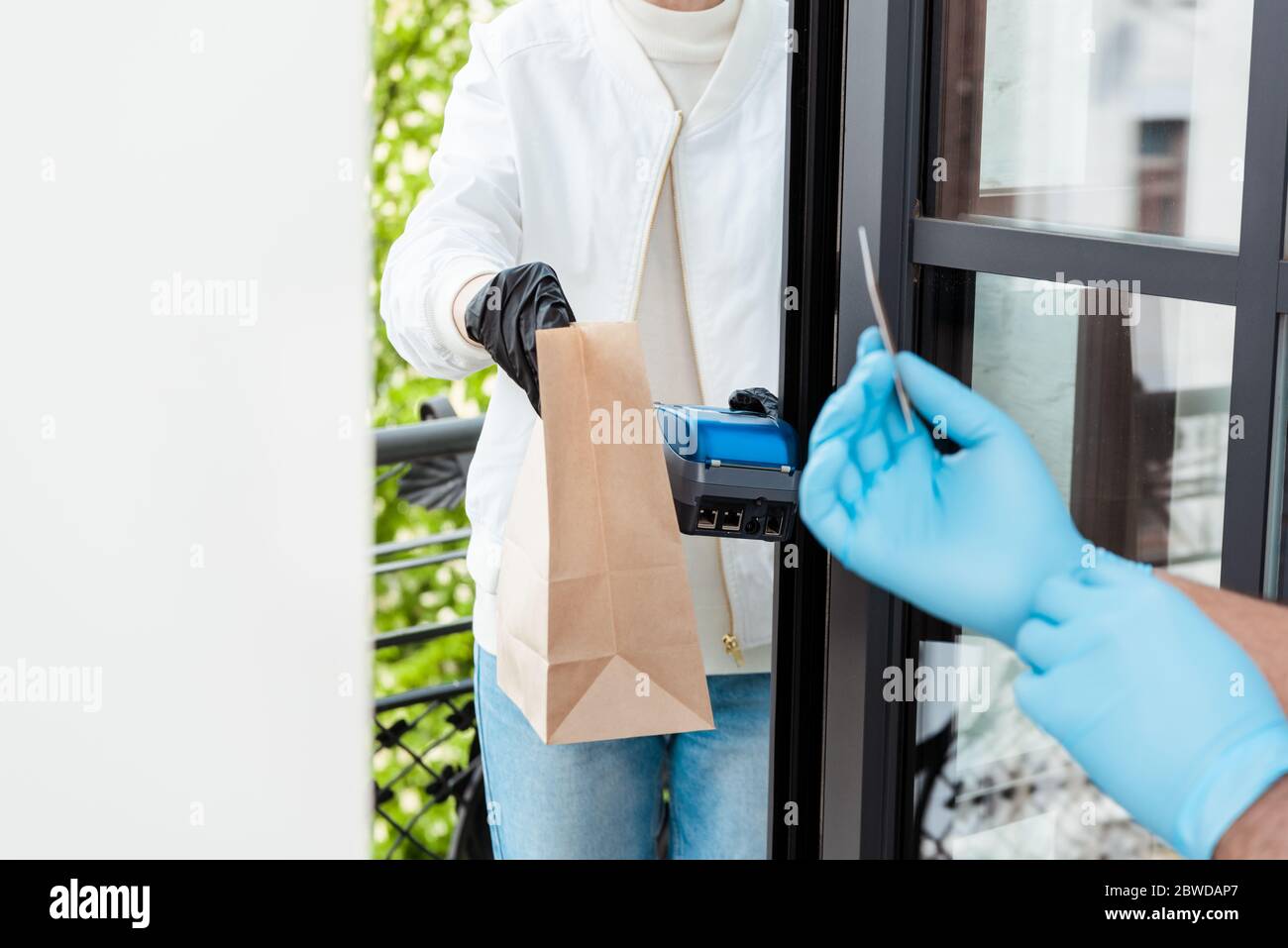 selective focus of delivery man holding credit card reader and paper bag near person in latex gloves with credit card Stock Photo