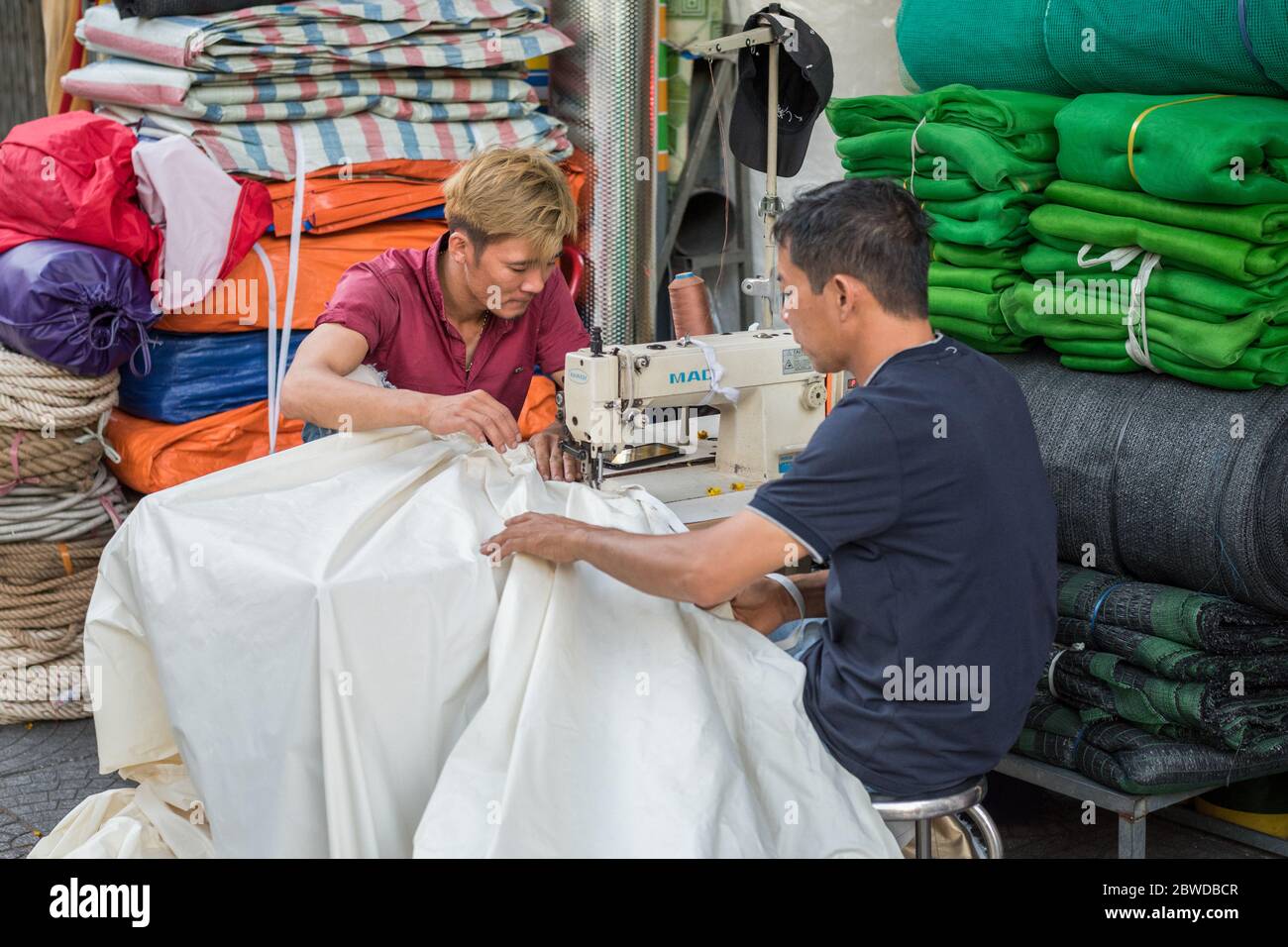 Ho Chi Minh City, Vietnam - February 11, 2019: Vietnamese men stitch a fabric with a sewing machine in the street near their small shop. Stock Photo