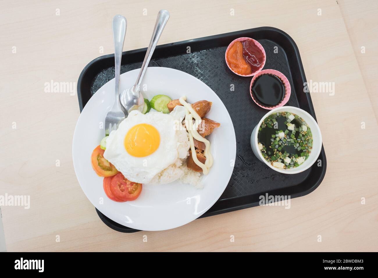 Meal at convenience store's canteen: fried egg and rice, a sausage, seaweed soup & fresh veggies. A closeup, a top-down view of plates on a tray. Stock Photo