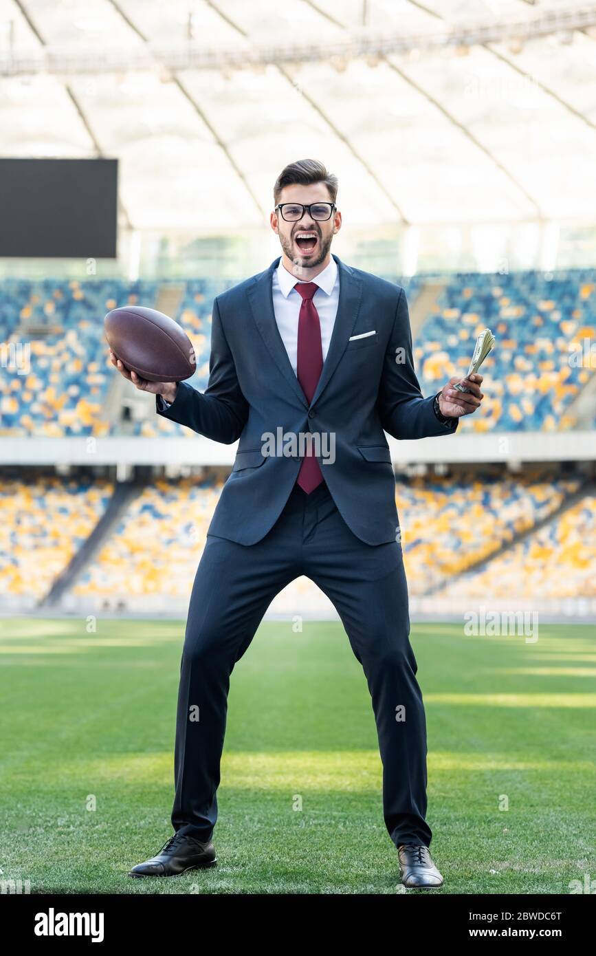 young businessman in suit and glasses with rugby ball yelling at