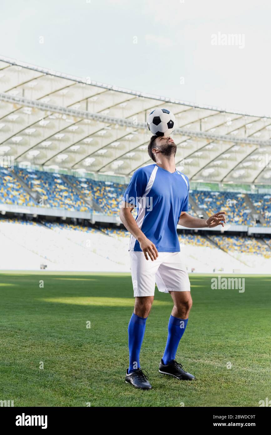 professional soccer player in blue and white uniform with ball on head at stadium Stock Photo