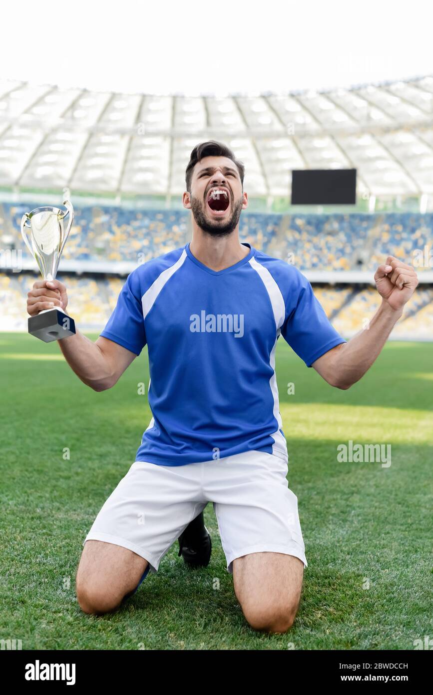 professional soccer player in blue and white uniform with sports cup