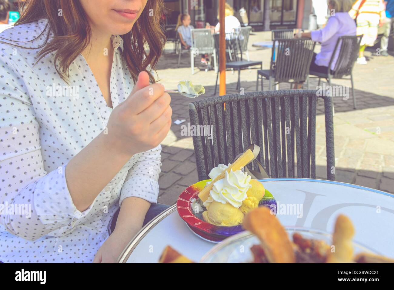 Caucasian happy woman holds spoon with ice cream, covered with  whipping cream and waffle. Cropped frame. Stock Photo