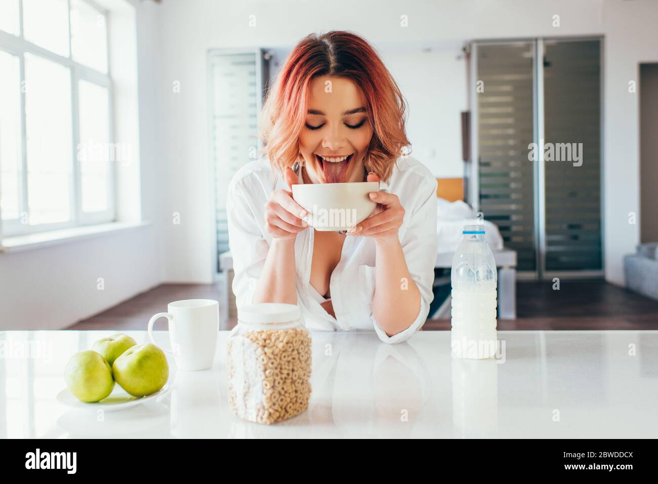 attractive funny girl licking cornflakes with milk during breakfast on self isolation Stock Photo