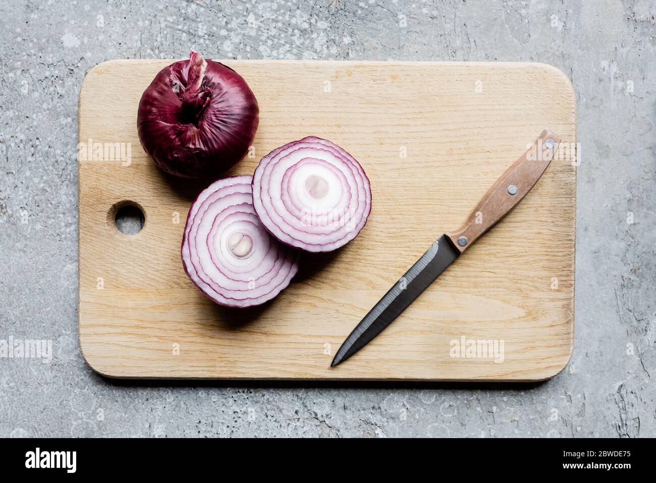 top view of onion on wooden cutting board with knife on grey concrete ...