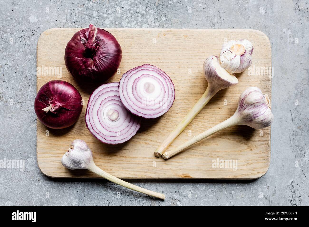 top view of onion and garlic on wooden cutting board on grey concrete ...