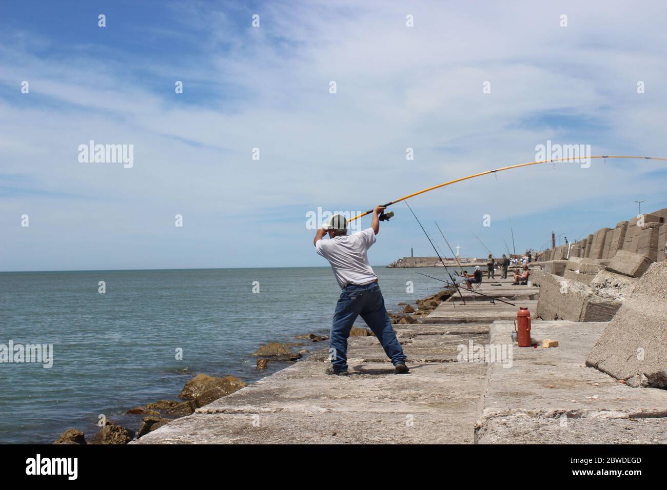 Fisherman throwing the fishing line and fishermen resting on the coast with Mate (Argentinean Tea) next to some stanks at the front and on the backgro Stock Photo