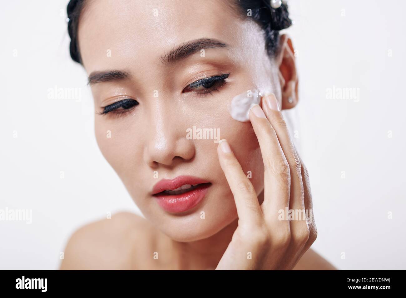 Beautiful young Vietnamese woman applying moisturizer on her face Stock Photo