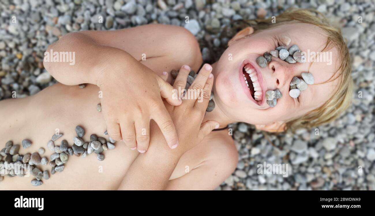 On sunny beach happy kids have fun, lying down on hot pebble, sunbathing, warming after swimming in sea. Active children lifestyle, summer vacation Stock Photo