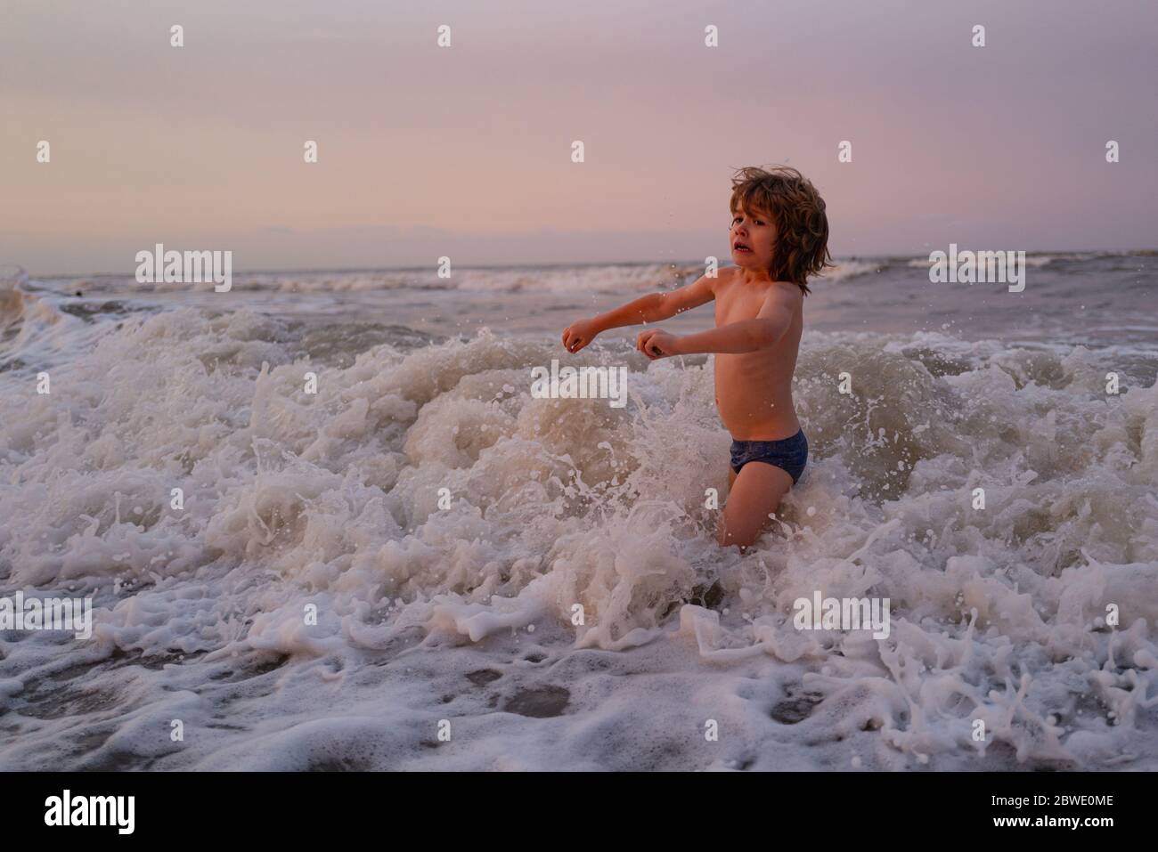 Kids jumping near the waves. Happy kids have fun in sea on beach. Travel lifestyle, swimming activities in family summer camp. Stock Photo