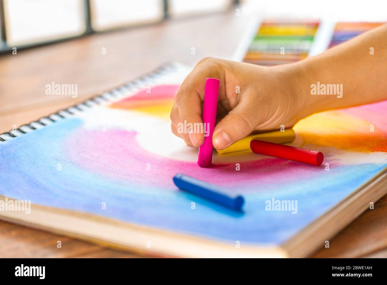 https://c8.alamy.com/comp/2BWE1AH/girls-hand-making-a-multi-colored-drawing-with-colorful-wax-crayon-on-a-sketch-pad-2BWE1AH.jpg