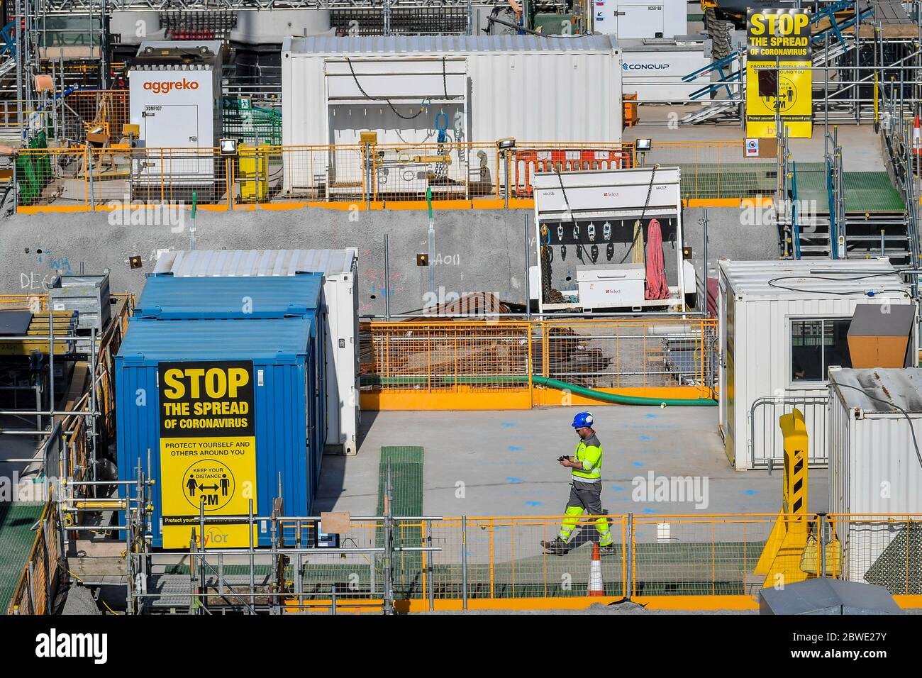 A construction worker passes between coronavirus advice signs at Hinkley Point C nuclear power station near Bridgwater, Somerset, Europe's largest building site, where they are completing a concrete pour into the base of unit 2 nuclear reactor. Stock Photo