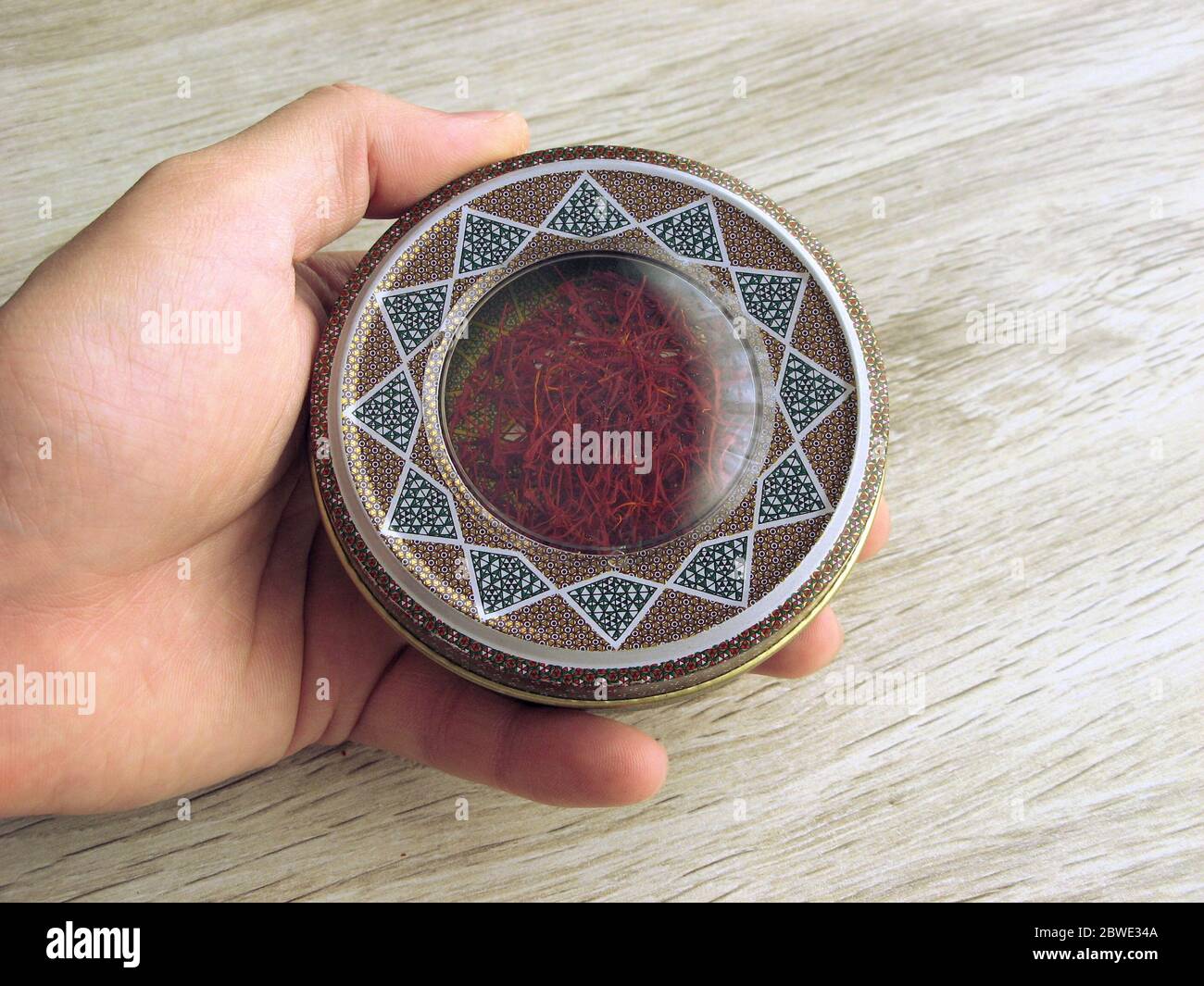 Mashhad, IRAN, 10 03 2020 Box containing red saffron in male hand on wooden background. Iranian
