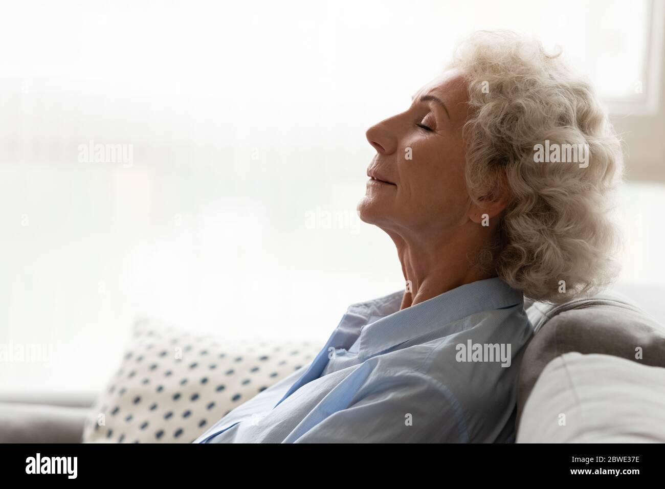 Peaceful old woman leaned on couch breathing fresh conditioned air Stock Photo