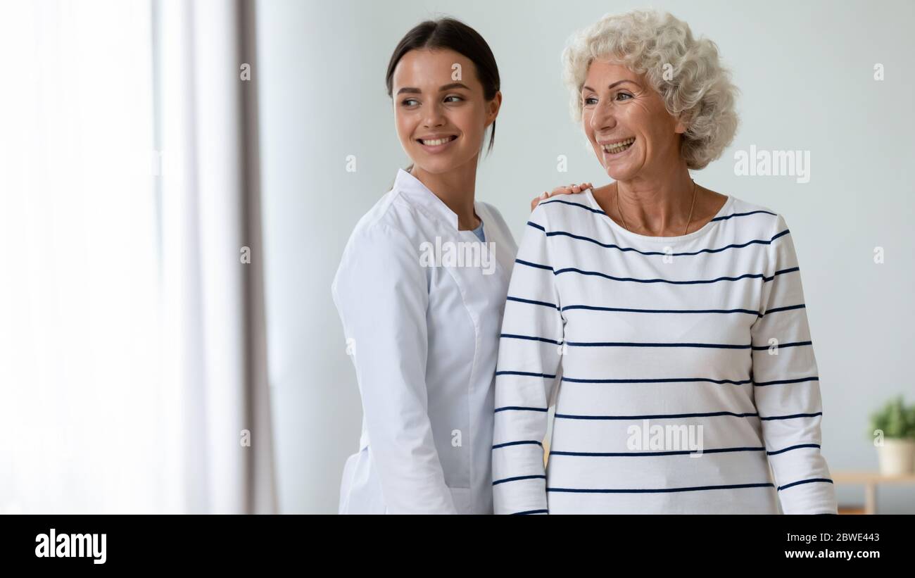 Caregiver and elderly patient standing together indoors looking in window Stock Photo