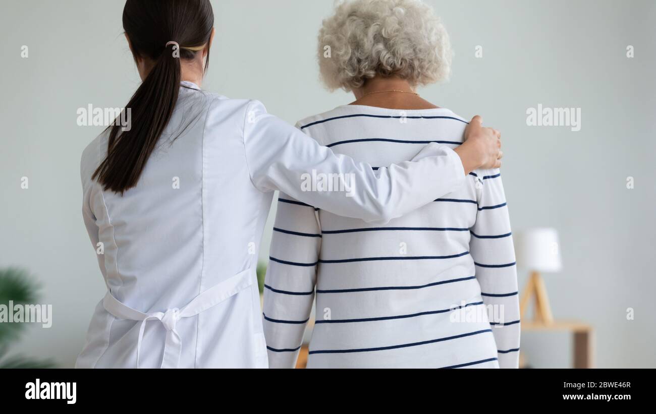 Rear view caregiver supporting helping to walk to elderly patient Stock Photo