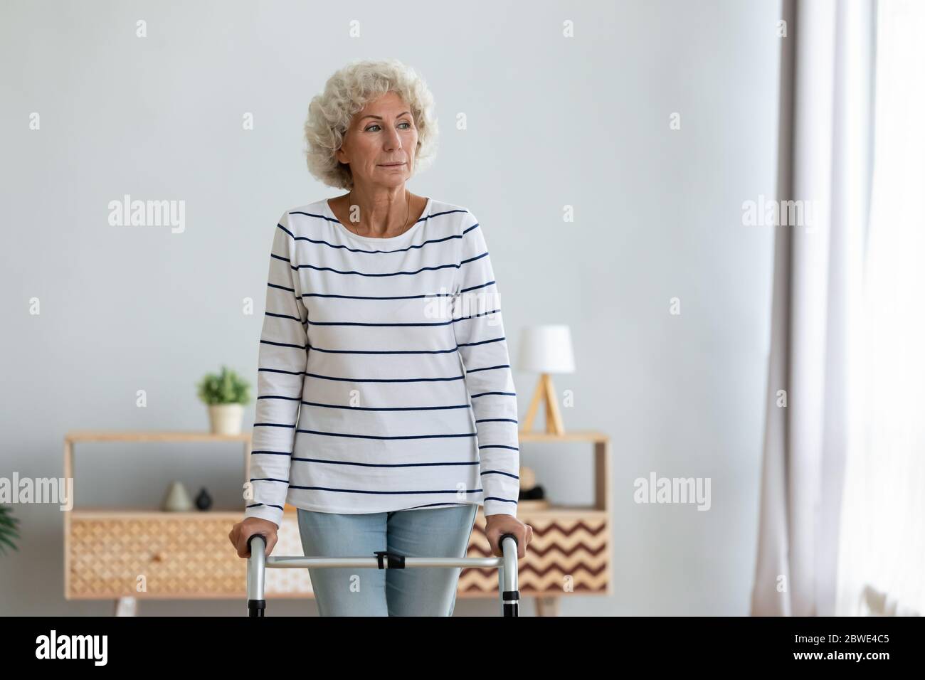 Elderly woman standing in living room holding walking frame Stock Photo