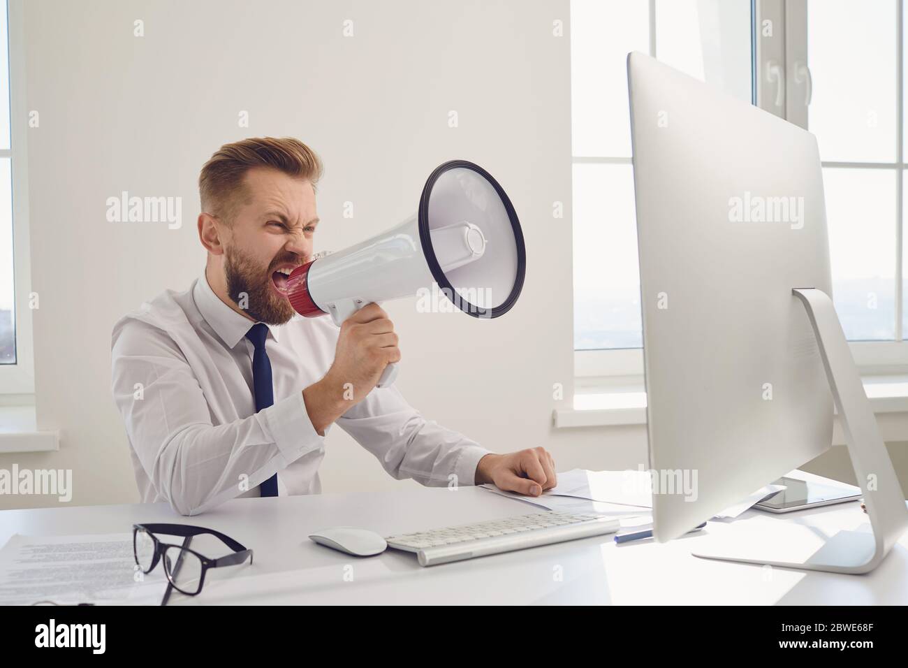 Angry displeased boss businessman shouting in megaphone into a computer Stock Photo