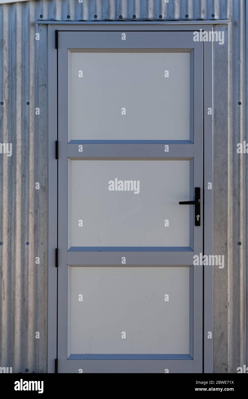 A metal door with a black handle set in a corrugated iron building Stock Photo