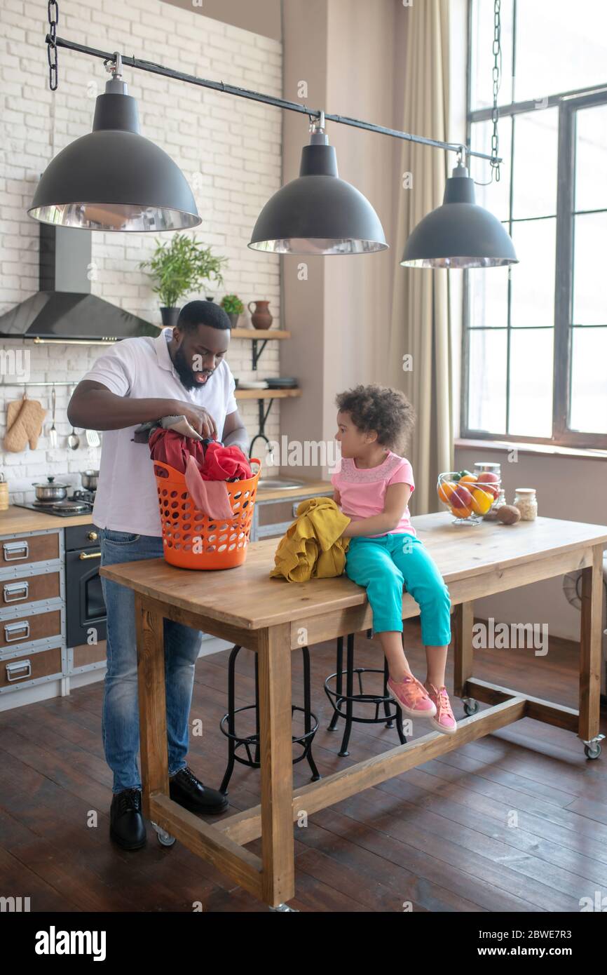 Dark-skinned tall father and his cute daughter looking busy with housework Stock Photo