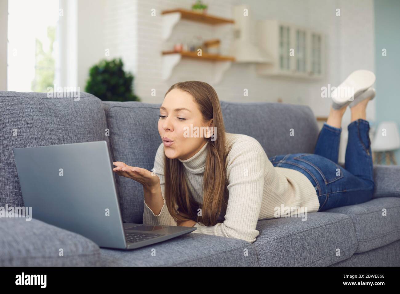 Dating online. Woman sending air kiss and using laptop in living chat room. Stock Photo