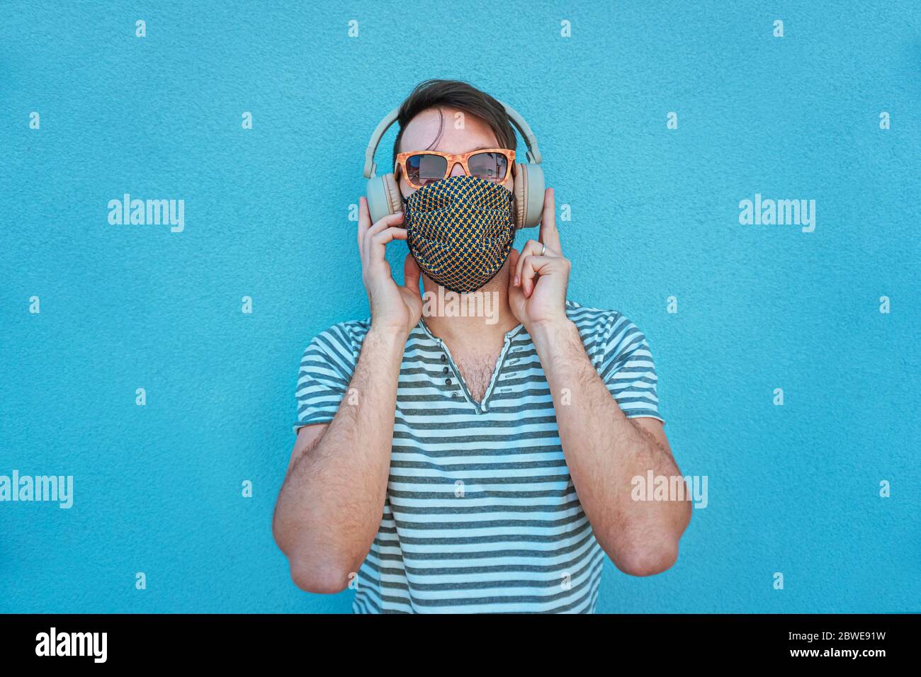 Boy with headphones on listening to music in covid-19 time with face mask and keeping the social distance Stock Photo
