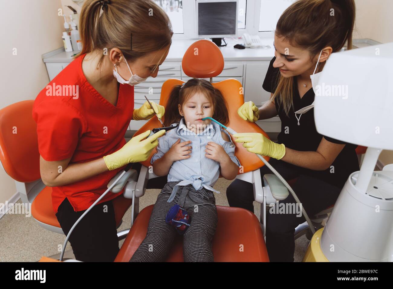 Female assistant using saliva ejector while dentist prepare to cure