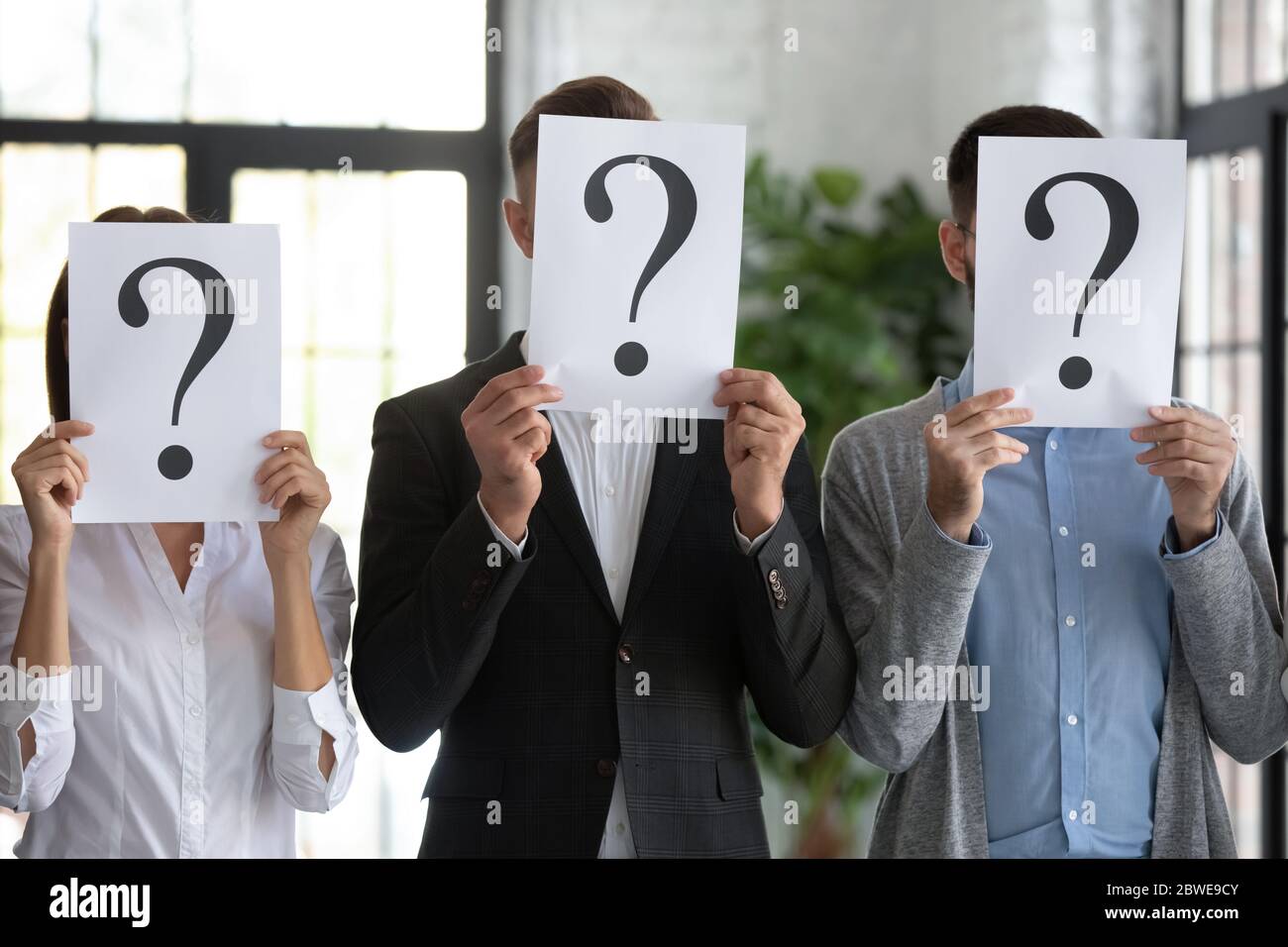 Close up workers hiding faces behind papers with question marks Stock Photo