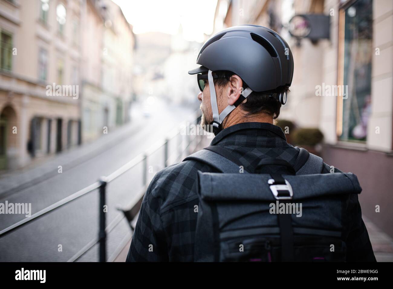 Rear view of delivery man courier with backpack and bicycle helmet in