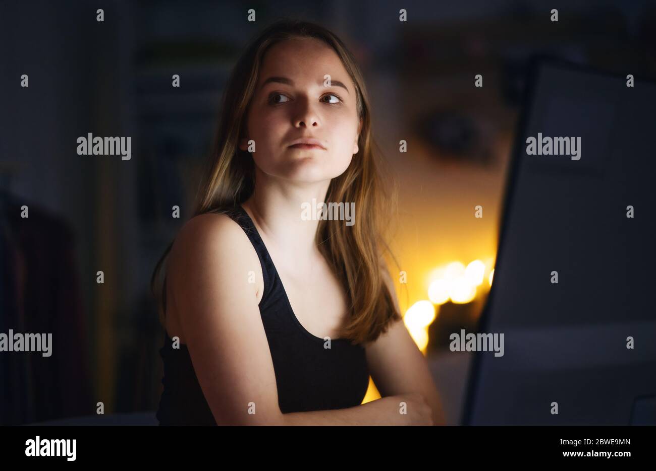 Worried young girl with computer sitting indoors, internet abuse concept. Stock Photo