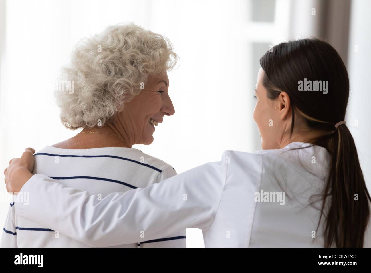 Caring nurse supporting hugging elderly woman clinic patient rear view Stock Photo