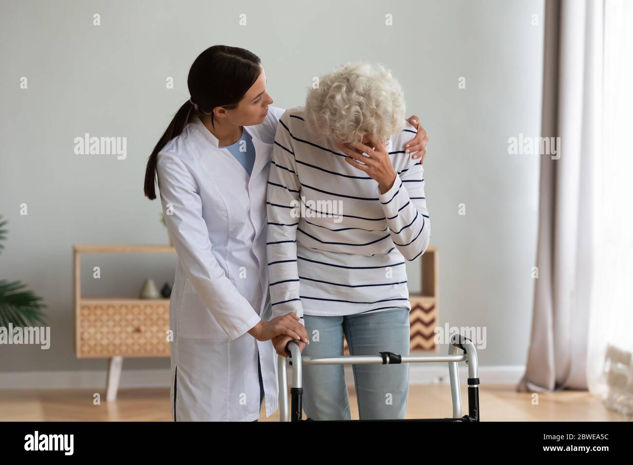 Caring nurse comforting unhappy aged disabled crying woman Stock Photo