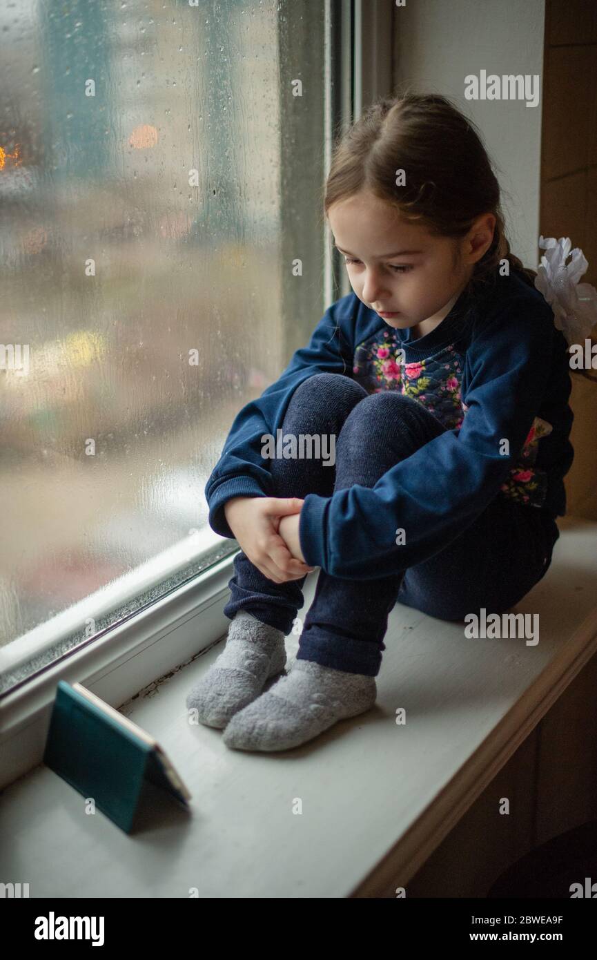 Beautiful cute female kid with sitting on windowsill. A little girl ...