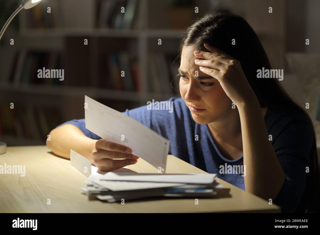 Worried woman looking at receipts at night sitting in the living room at home Stock Photo