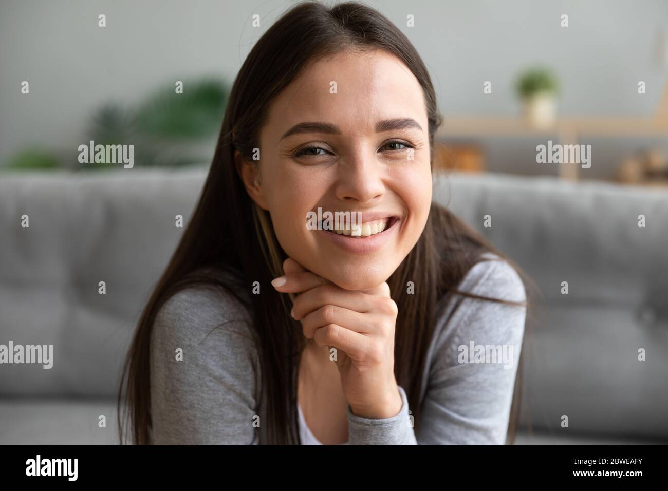 Beautiful young woman sit on couch smiles looks at camera Stock Photo