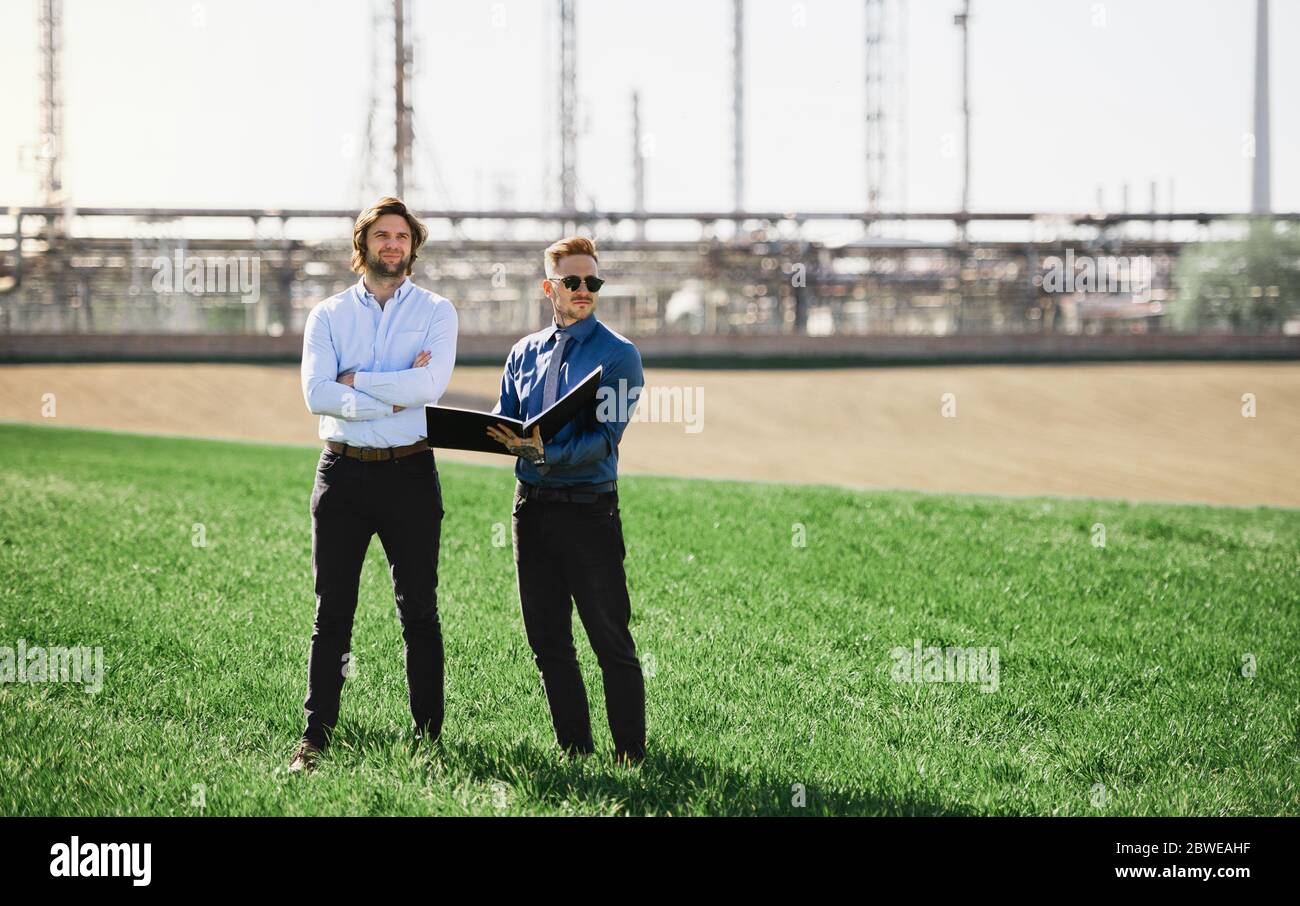Two young engineers standing outdoors by oil refinery, discussing issues. Stock Photo
