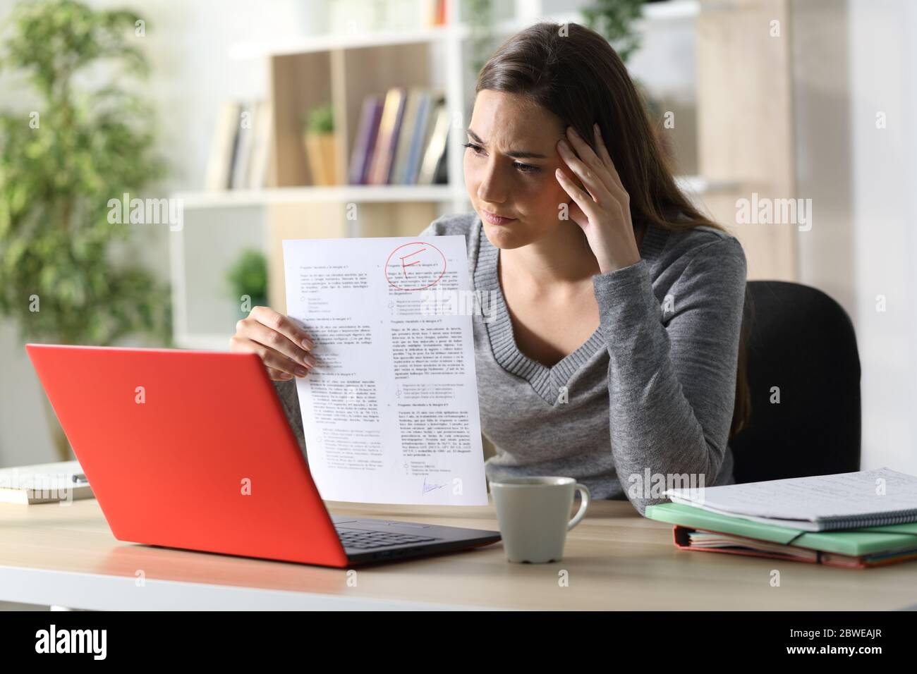 Sad student woman showing failed exam on videocall on laptop sitting on a desk at home Stock Photo