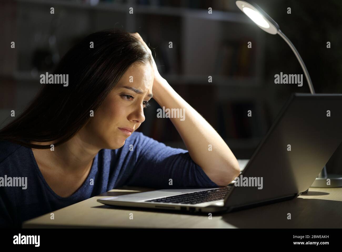 Sad woman looking at laptop complaining sitting alone at night at home Stock Photo
